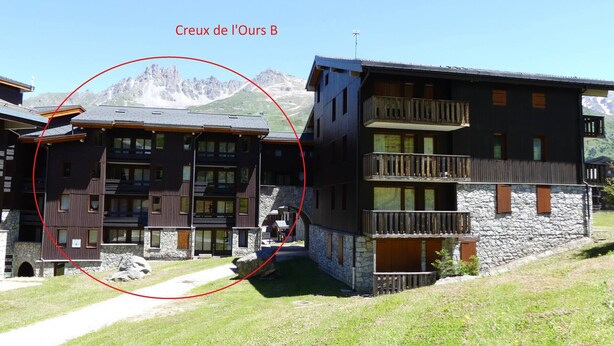 Un edificio moderno con fachada de piedra y varios balcones, rodeado de un paisaje montañoso.