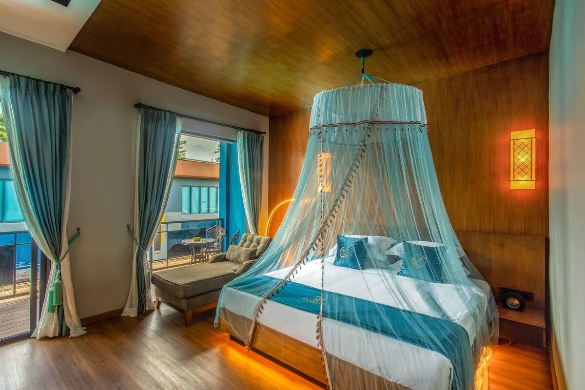 A bedroom with a bed under a canopy, a sofa, and a view of the outside.