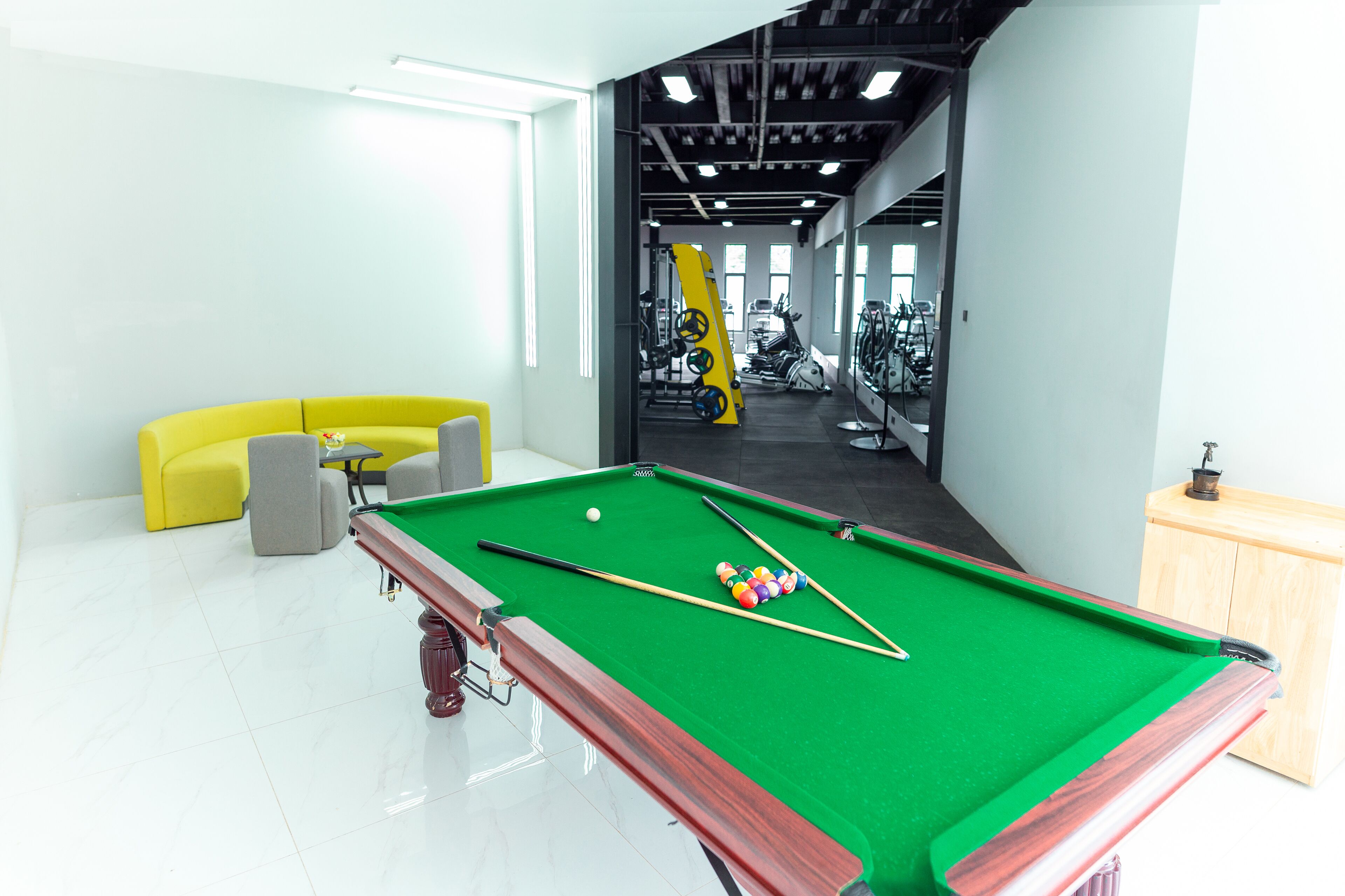 Une table de billard dans une pièce lumineuse, avec un canapé jaune et du matériel de sport en arrière-plan.
