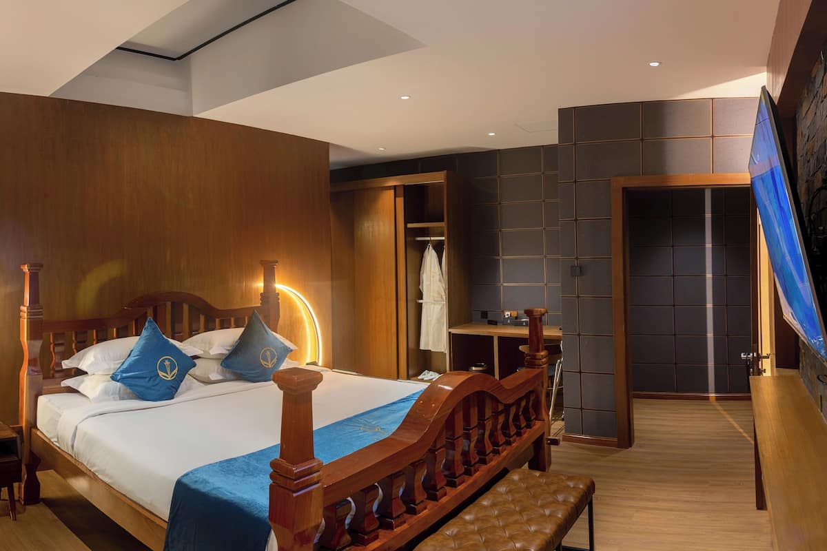A modern hotel room with a wooden bed, a bench, a desk, and a wardrobe.