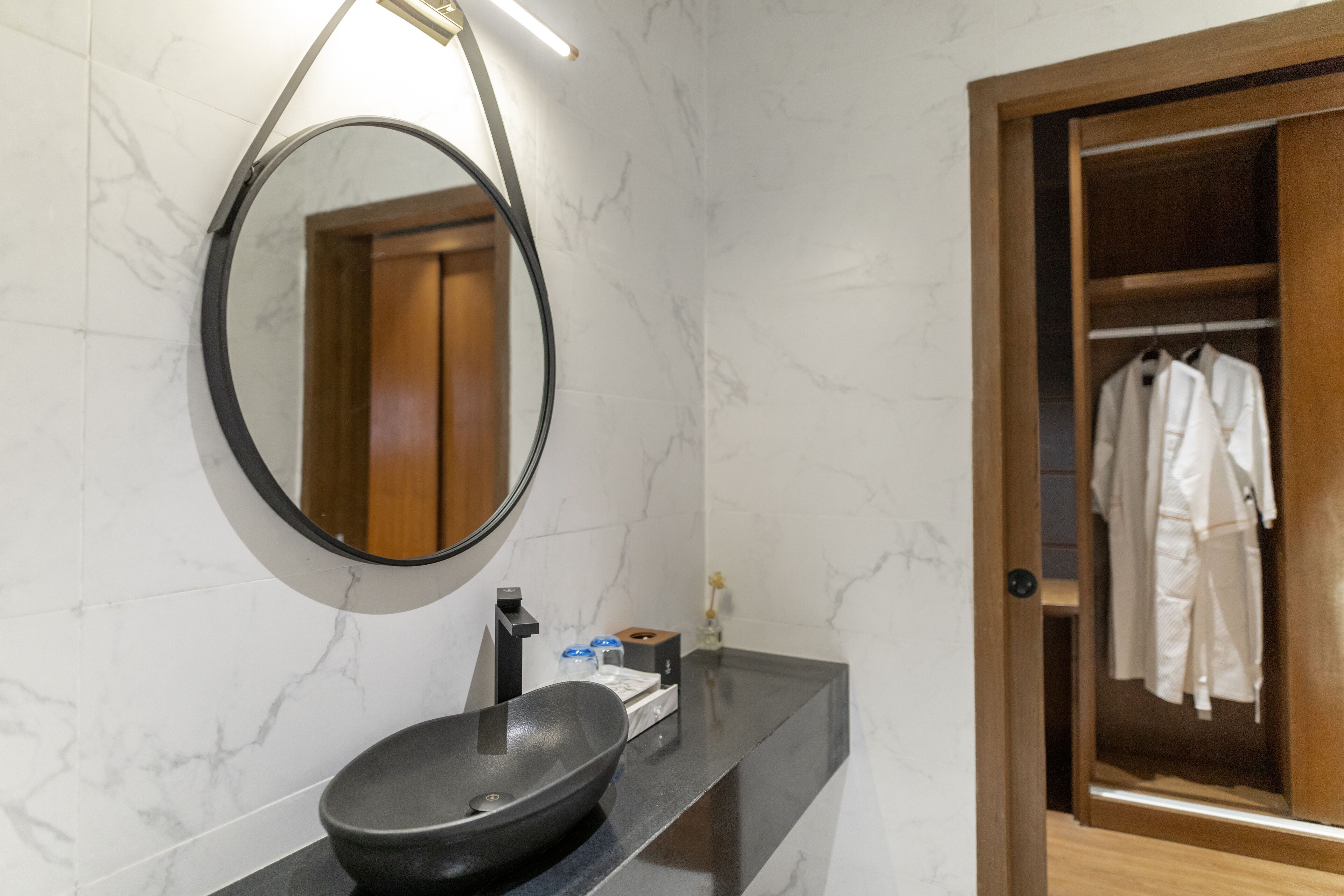 A bathroom with a round mirror, black sink, and marble walls.
