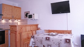 Une cuisine compacte avec des meubles en bois, un four à micro-ondes et un téléviseur à écran plat fixé au mur.
