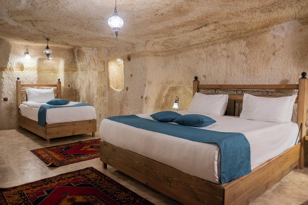 A rustic room with two wooden beds, each with a blue blanket and pillows, and a patterned rug on the floor.