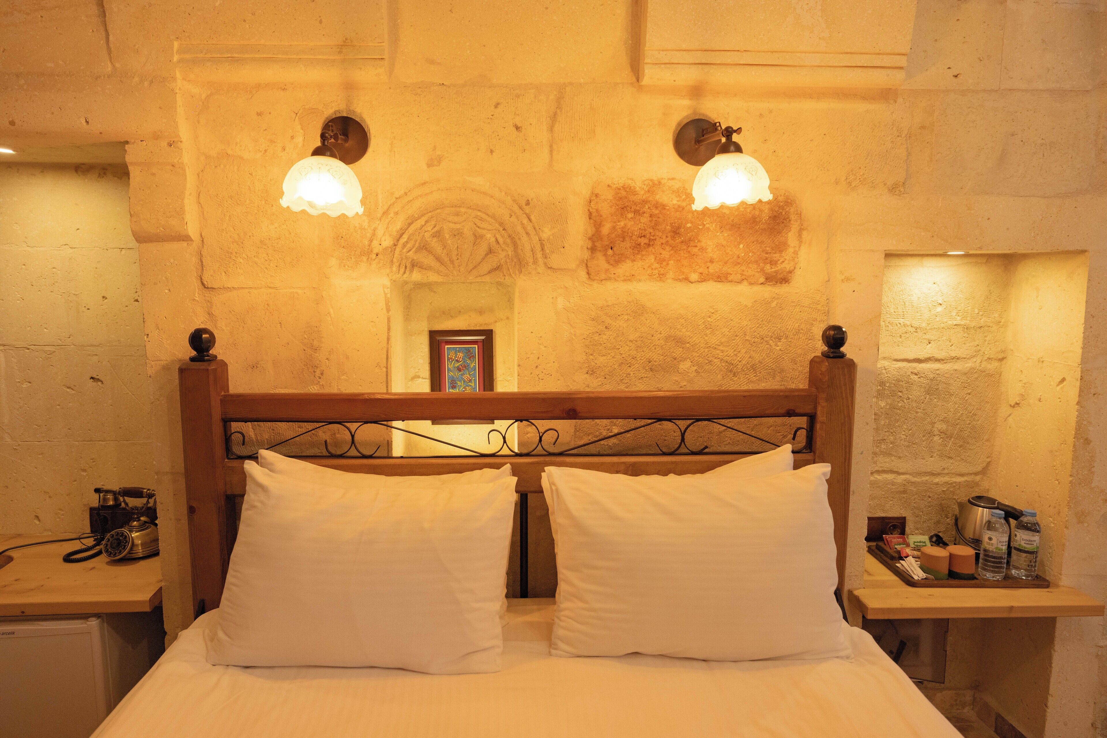 A bed with two pillows, a wooden headboard, and two wall-mounted lamps.