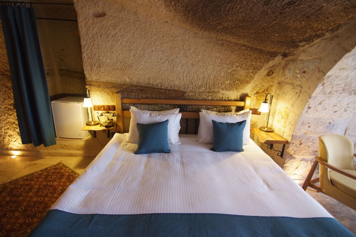 A bedroom with a large bed, two bedside tables with lamps, a chair, and a rustic stone ceiling.