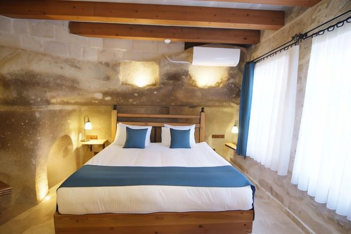 A bedroom with a wooden bed, stone walls, and a window with curtains.