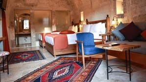 A rustic room with a large bed, a wooden chair, a small table, and a sofa. There is a mirror, a sink, and a window. - Peruna Cave (Nevsehir)