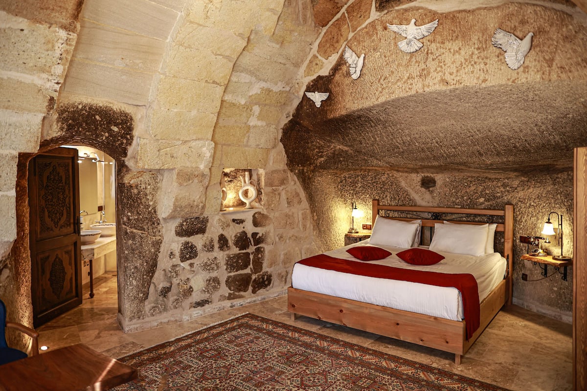 A rustic bedroom with a stone wall, wooden bed, and a red throw blanket.