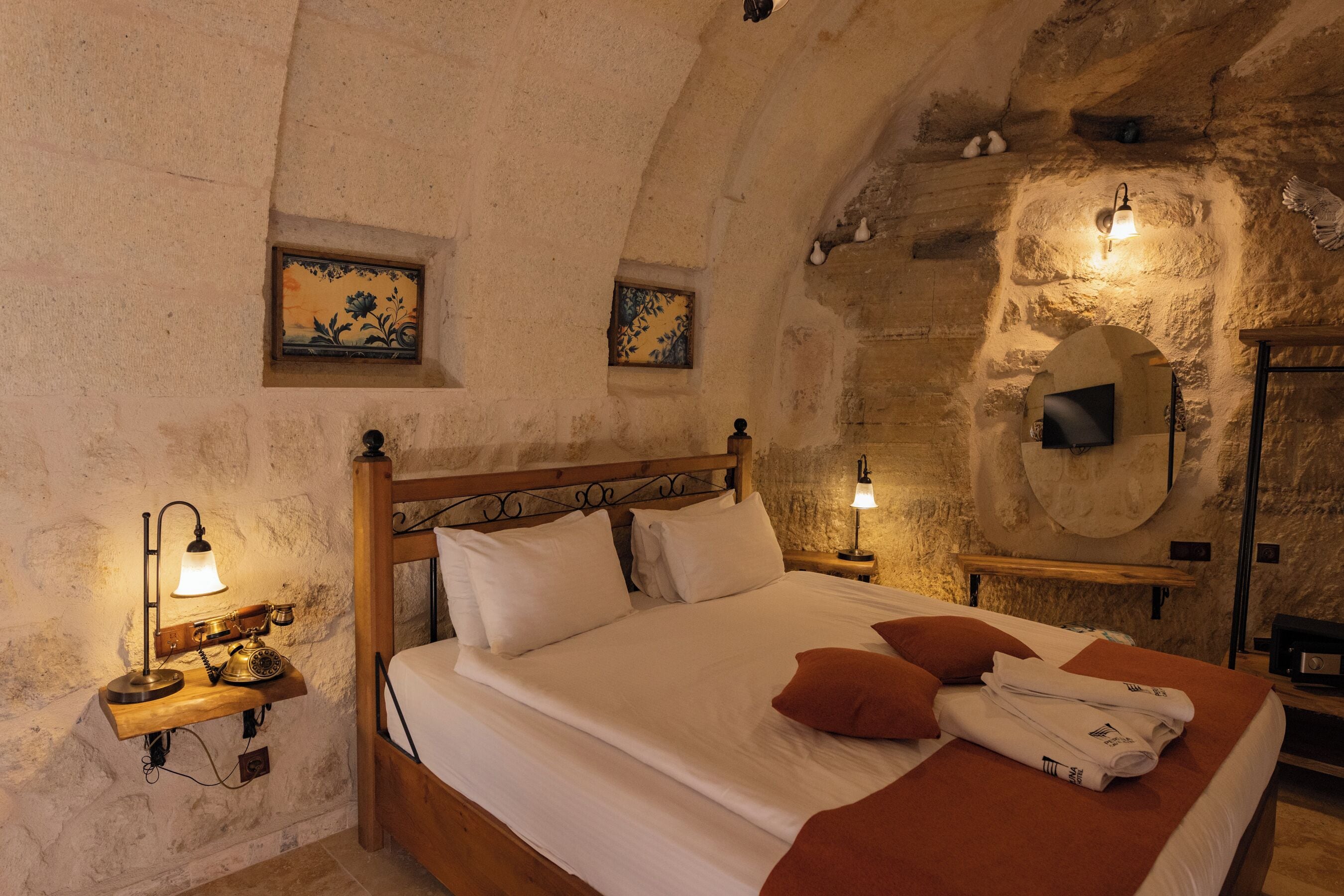 A cozy room with a wooden bed, a nightstand with a lamp, and a stone wall.