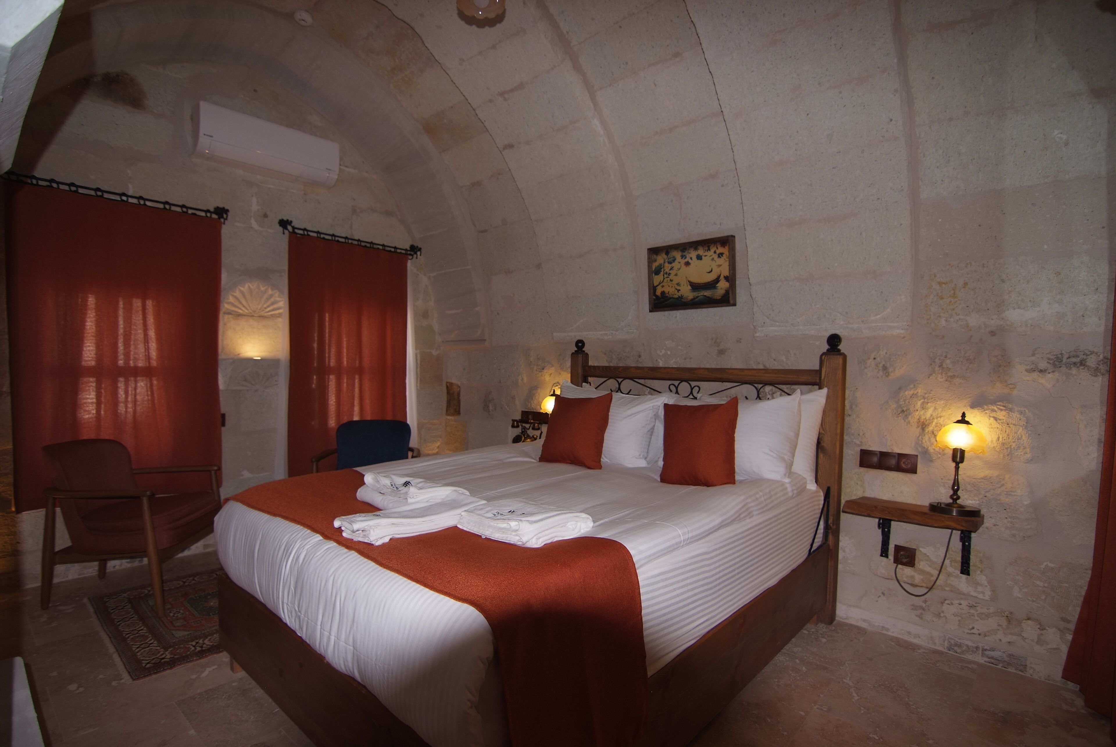 A bedroom with a large bed, two bedside tables with lamps, a chair, and a wall-mounted shelf.
