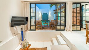A modern living room with a large TV, a sofa, and a view of an outdoor pool area. - Villa The View (Canggu)