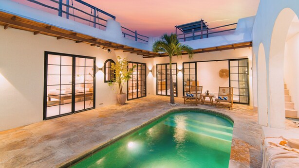 A pool area with a view of the sunset, a palm tree, and a seating area with chairs and a table. - Villa The View (Canggu)