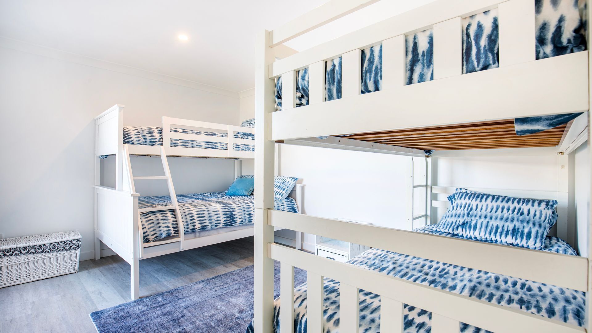 A bunk bed room with a ladder, a woven basket, and a blue rug.