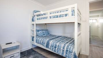 Una cama litera con una colcha azul y blanca estampada, una mesita de noche con un control remoto y una alfombra gris en el suelo.