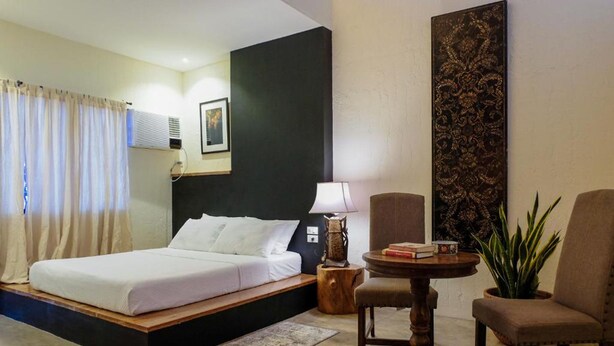 A bedroom with a bed, a bedside table with a lamp, a chair, and a potted plant. - Ceda Guest House by HiveRooms (Santa Fe)