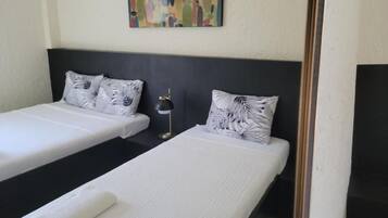 A hotel room with two single beds, each with a white bedspread and a leaf-patterned pillow. A black headboard separates the beds, and a colorful abstract painting hangs on the wall above.