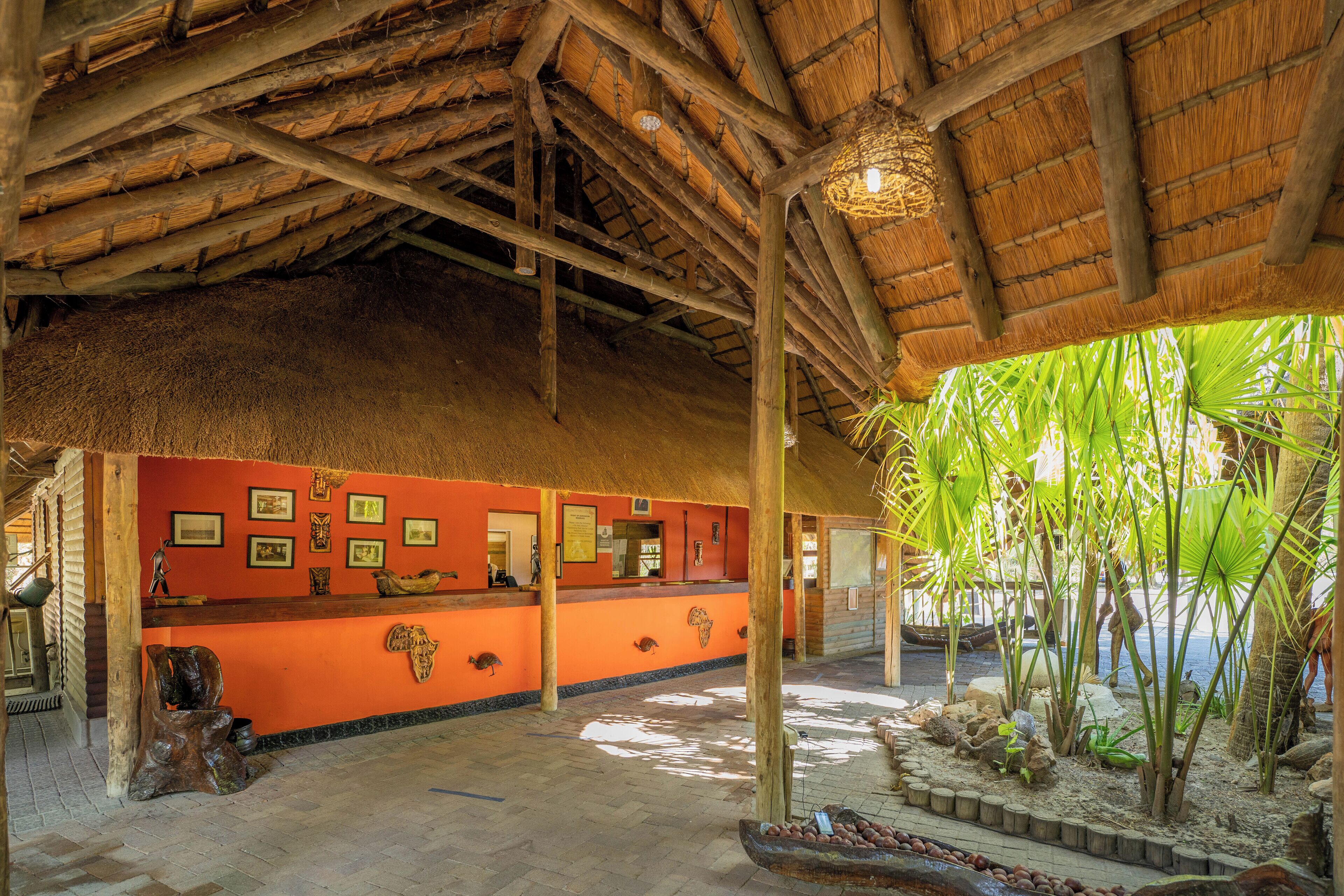 An interior with a thatched roof, a reception desk, framed pictures, and a tropical plant area.