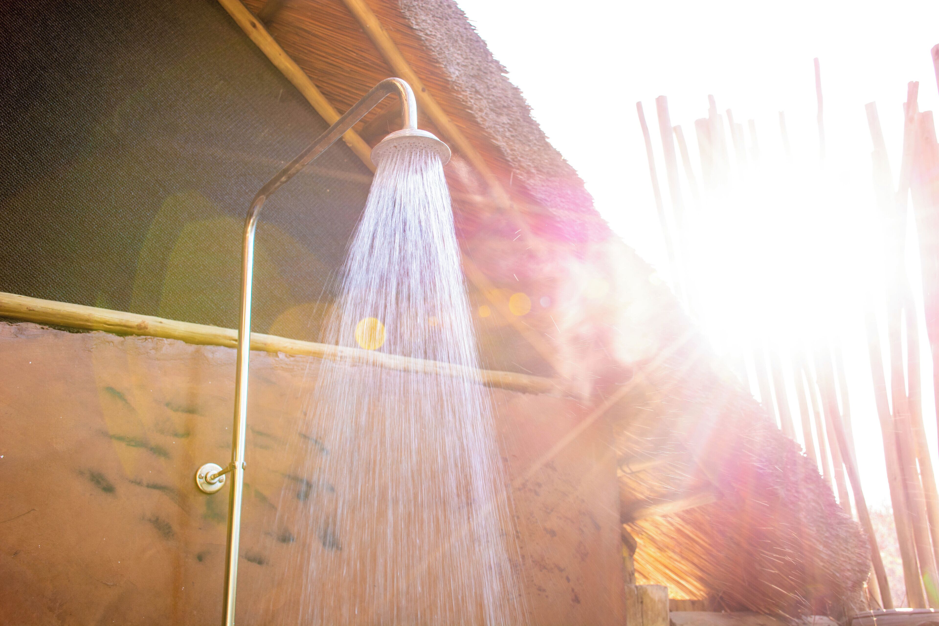 Une douche où l’eau coule d’un robinet en métal, le tout installé sur un mur à surface texturée.