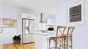 Una cocina moderna con armarios blancos, electrodomésticos de acero inoxidable y una isla central con taburetes de bar.