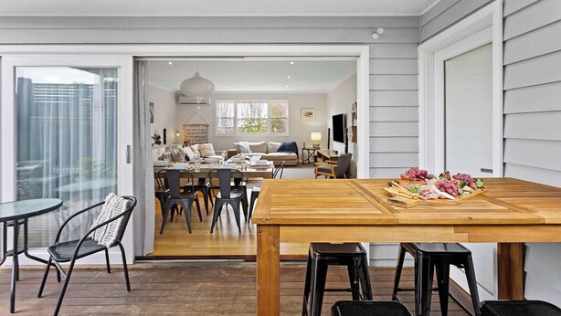 Amplia sala de estar con mesa de comedor de madera, sillas negras y vista hacia la cocina.