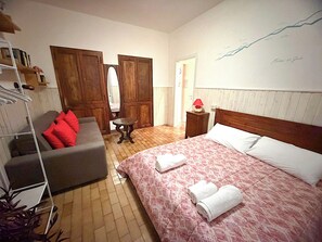 A hotel room with a bed, a sofa, a wooden wardrobe, a small table, and a wall with a simple design. - Lake Como Breva (Bellagio)