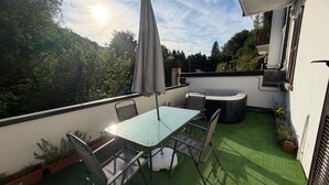 Um pátio com mesa e cadeiras, uma banheira de hidromassagem e vista para árvores e colinas.