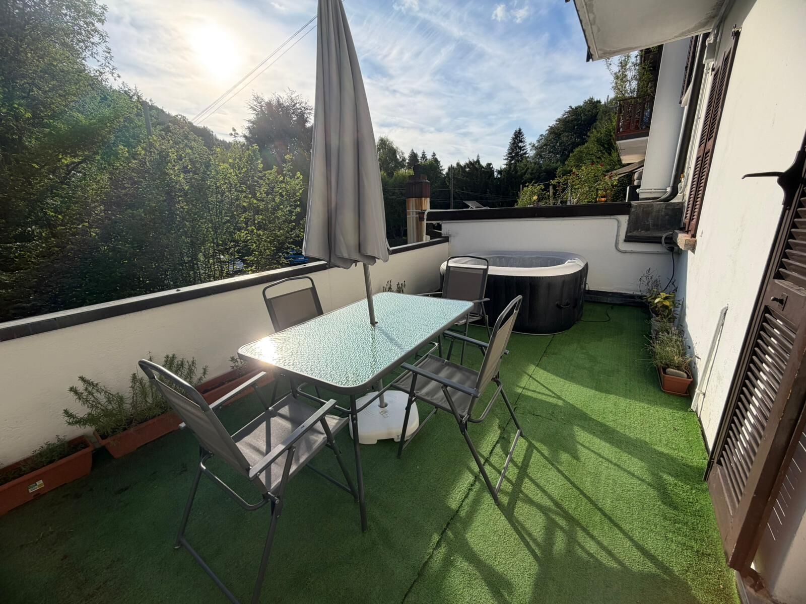 A rooftop terrace with a table and chairs, a hot tub, and potted plants.