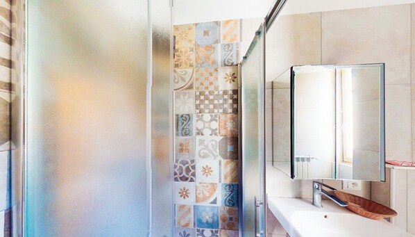 Un baño con pared de ducha azulejada, un espejo y un mueble de tocador de madera.