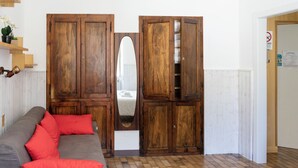 Quarto com guarda-roupa de madeira, sofá cinza com almofadas vermelhas e porta branca com placa de 'Não Fumar'.