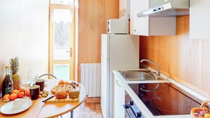 Cozinha compacta com pia, micro-ondas e fogão. Uma mesa exibe frutas, nozes e uma garrafa.