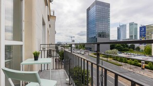 Un balcón con mesa y sillas, con vista a una calle de la ciudad con edificios modernos y una autopista.