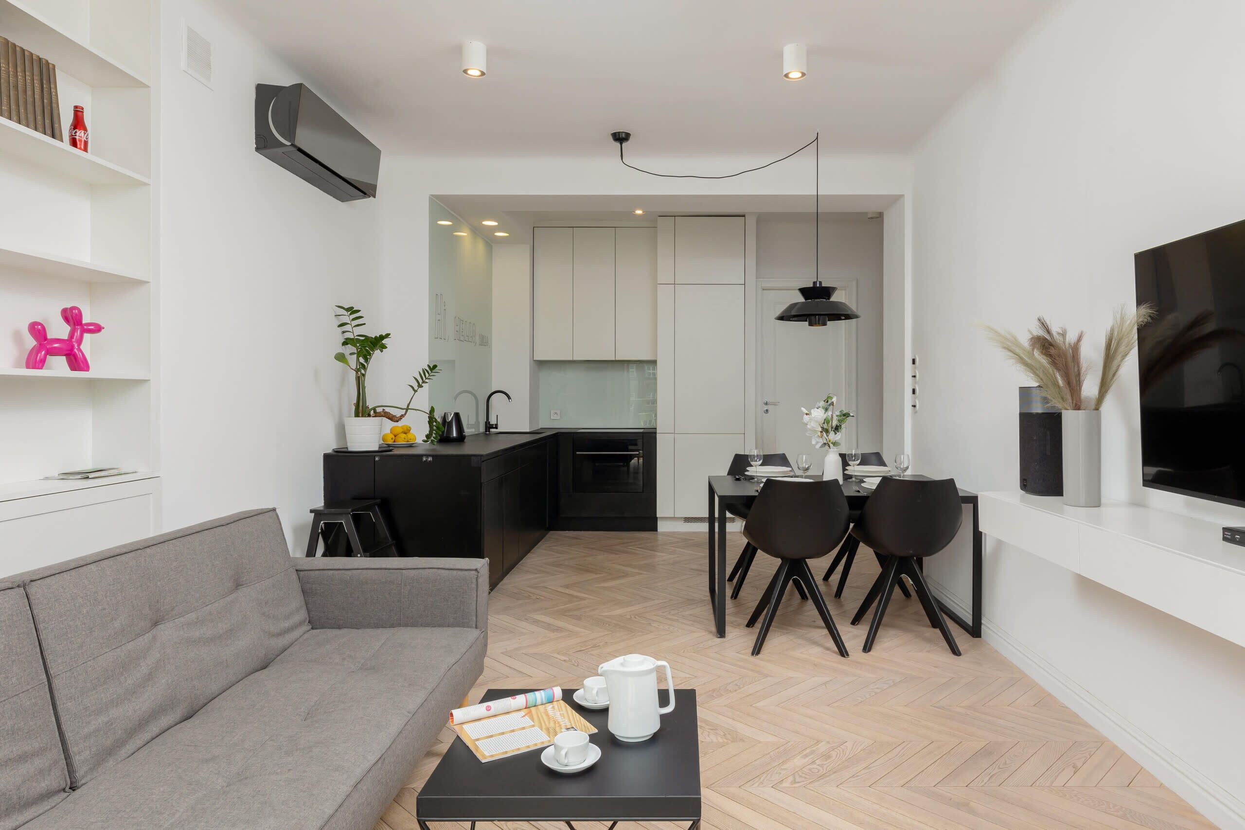 A modern living room with a grey sofa, a black coffee table with a tray, and a dining area with a black table and chairs.