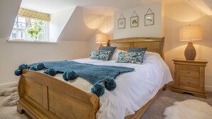 A bedroom with a wooden bed, white bedding, a blue knitted throw, and a nightstand with a lamp. - The Vicarage Cottage -  an idyllic cottage in Great Limber sleeping 4 guests (Great Limber)