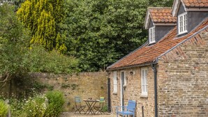 A stone building with a tiled roof, a brick wall, and a small patio area with a table and chairs. - The Vicarage Cottage -  an idyllic cottage in Great Limber sleeping 4 guests (Great Limber)