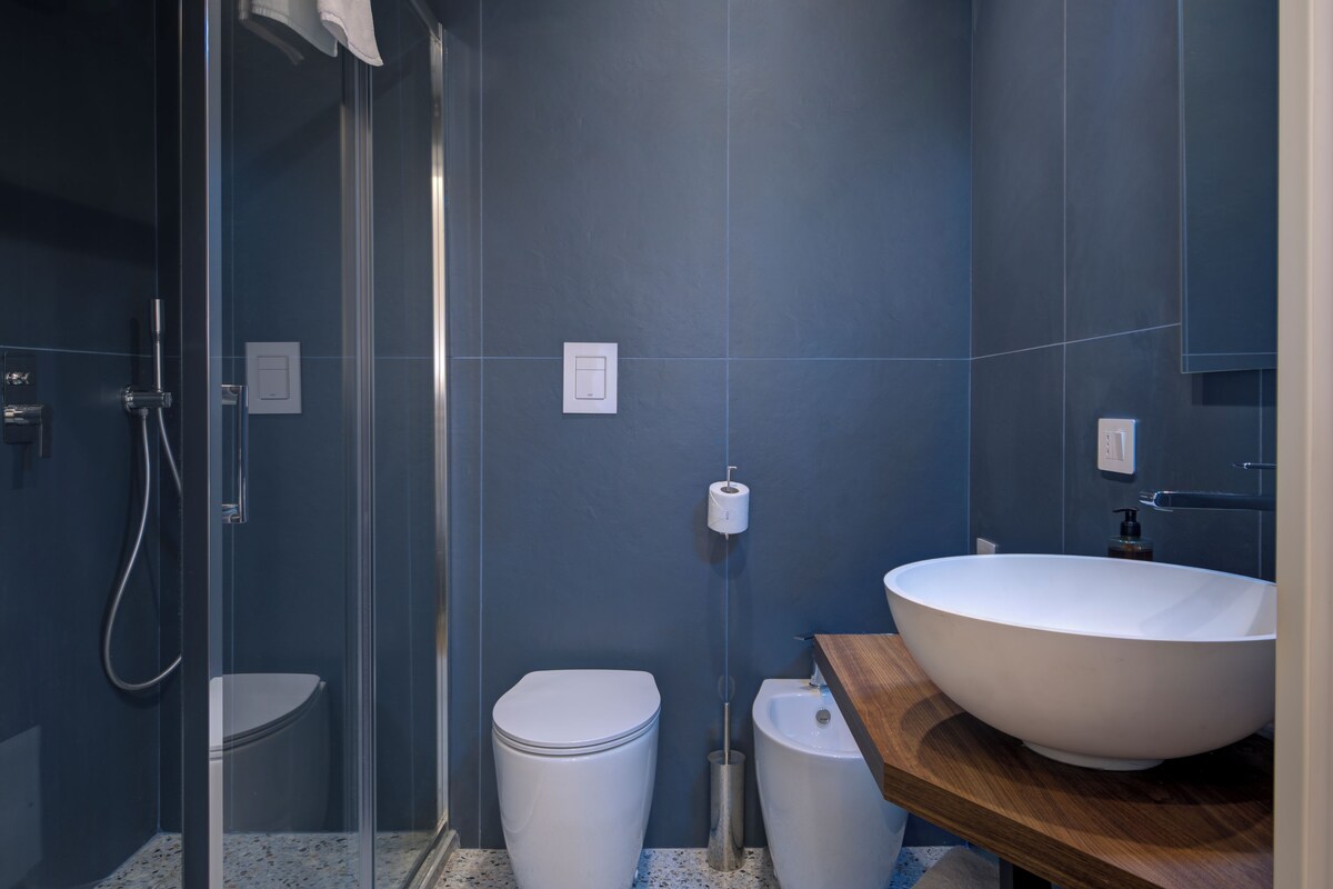 A modern bathroom with a glass-enclosed shower, a white toilet, and a large vessel sink on a wooden countertop.