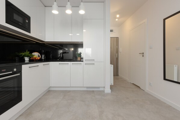 Cocina moderna con armarios blancos, electrodomésticos negros y una isla central. Hay luces colgantes sobre la isla y un microondas sobre el horno.