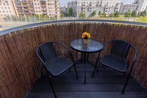 Un balcón con dos sillas de mimbre negro y una mesita redonda con un centro de mesa de flores amarillas.