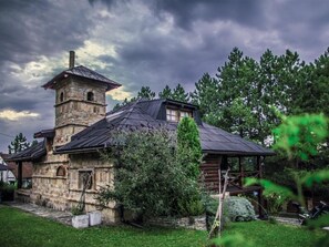 A rustic stone building with a tower, a covered porch, and a well-maintained garden.