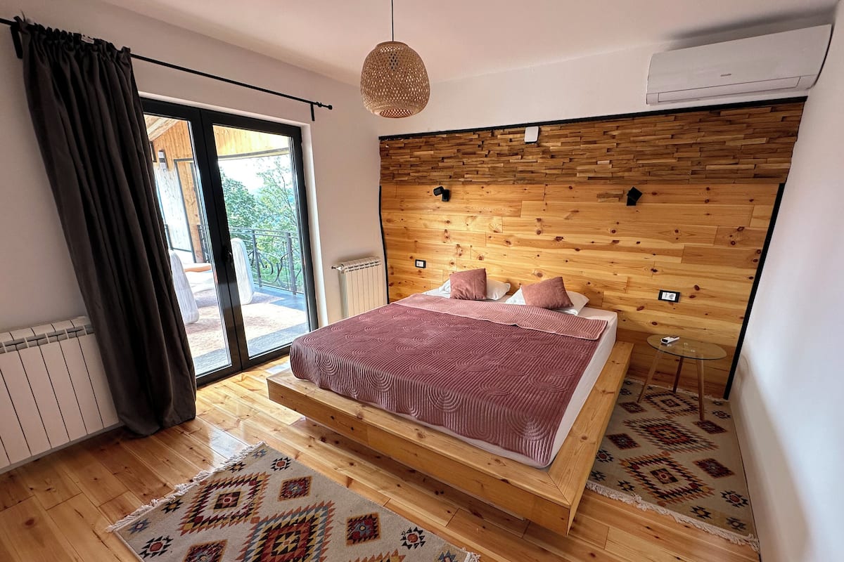 Un dormitorio con cabecera de madera, una cama grande, una mesita pequeña y un tapete estampado.