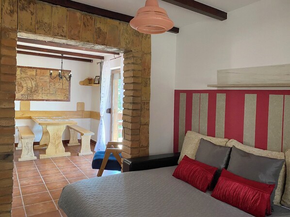 A bedroom with a bed, a wooden bench, a table, and a stone wall.