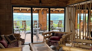 A spacious room with bamboo furniture, large windows, and a view of a lush landscape. - Zdravkovac Country Club (Topola)