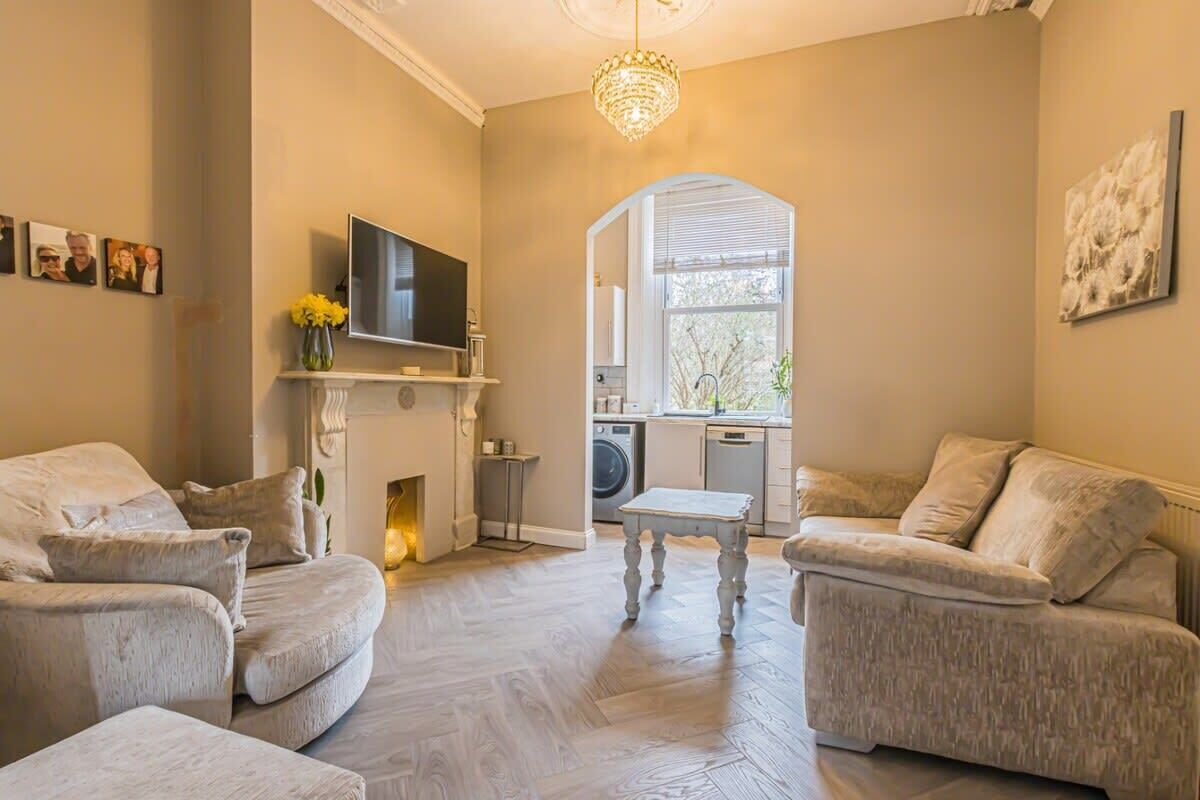 A living room with two sofas, a television, a fireplace, and a kitchen area visible through an archway.