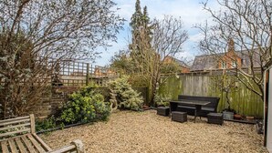 A gravel patio with a wooden bench and a table, surrounded by plants and a wooden fence. - Ground Floor 1 Bedroom Flat - Windsor By Tempstay (Berkshire)