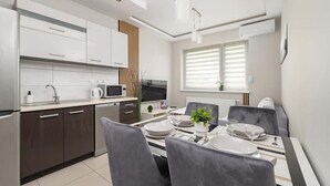 A modern kitchen with white cabinets, a dining table set for four, and a large window with blinds.