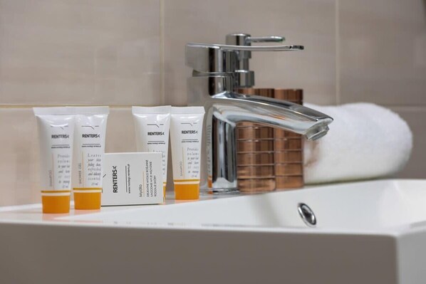 Un baño con grifo cromado, lavabo blanco y artículos de aseo que incluyen un tubo de crema y una botella de loción.