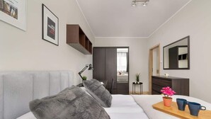 A modern bedroom with a large bed, a bedside table with a lamp, a dresser, and a mirror.