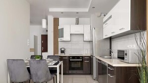 A modern kitchen with white cabinets, stainless steel appliances, and a dining area with grey chairs and a white table.
