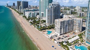 An aerial view of a coastal city with a beachfront hotel featuring a swimming pool, multiple buildings, and a clear view of the ocean. - Deluxe 1-bed 2-bath ocean front free valet parking on the beach (Hollywood)