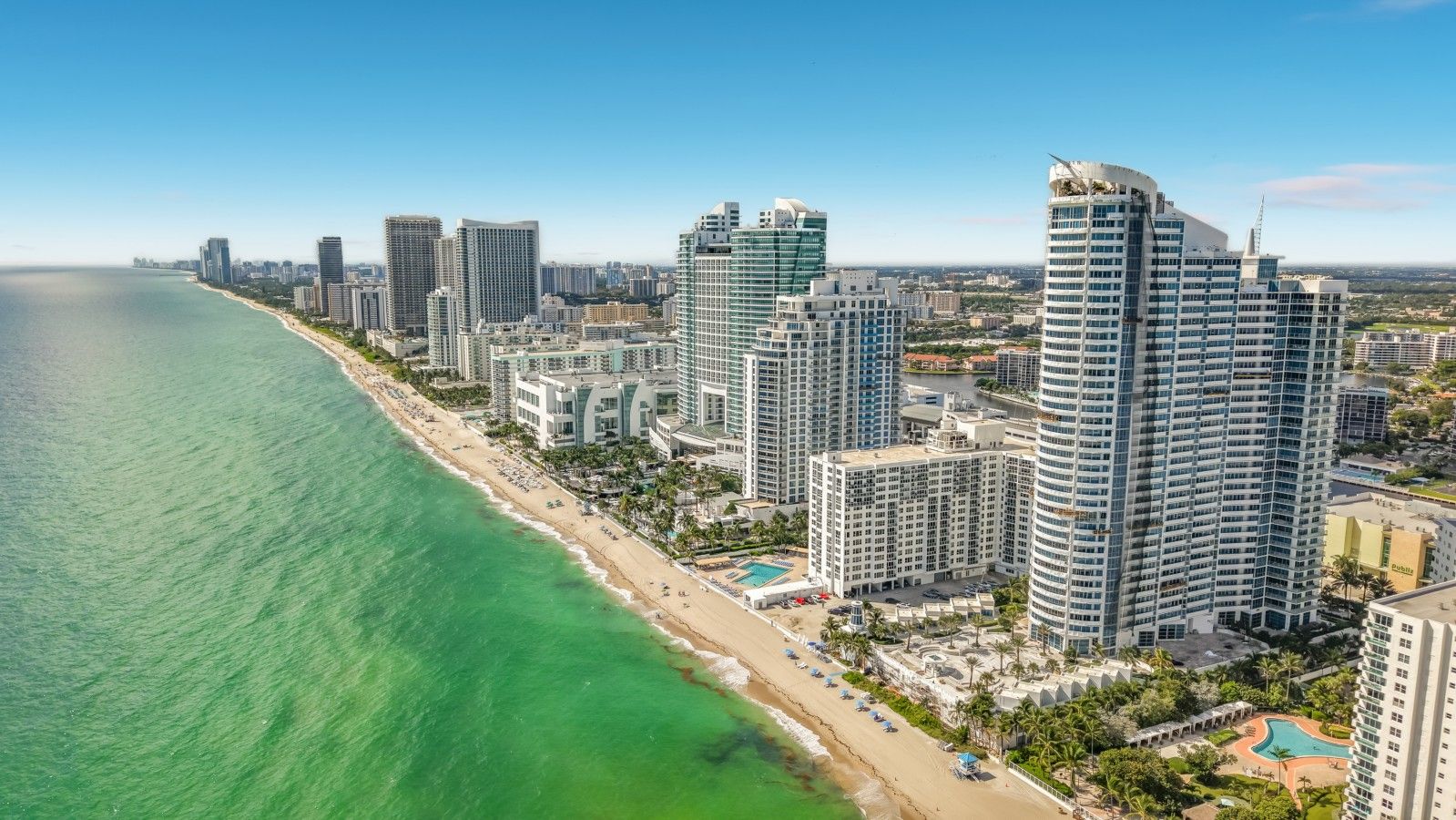 Un paysage urbain côtier avec de hauts immeubles, une plage et un ciel dégagé.