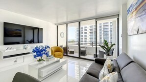 A modern living room with a flat-screen TV, a sofa, a yellow armchair, and a large window with a city view. - Deluxe 1-bed 2-bath ocean front free valet parking on the beach (Hollywood)